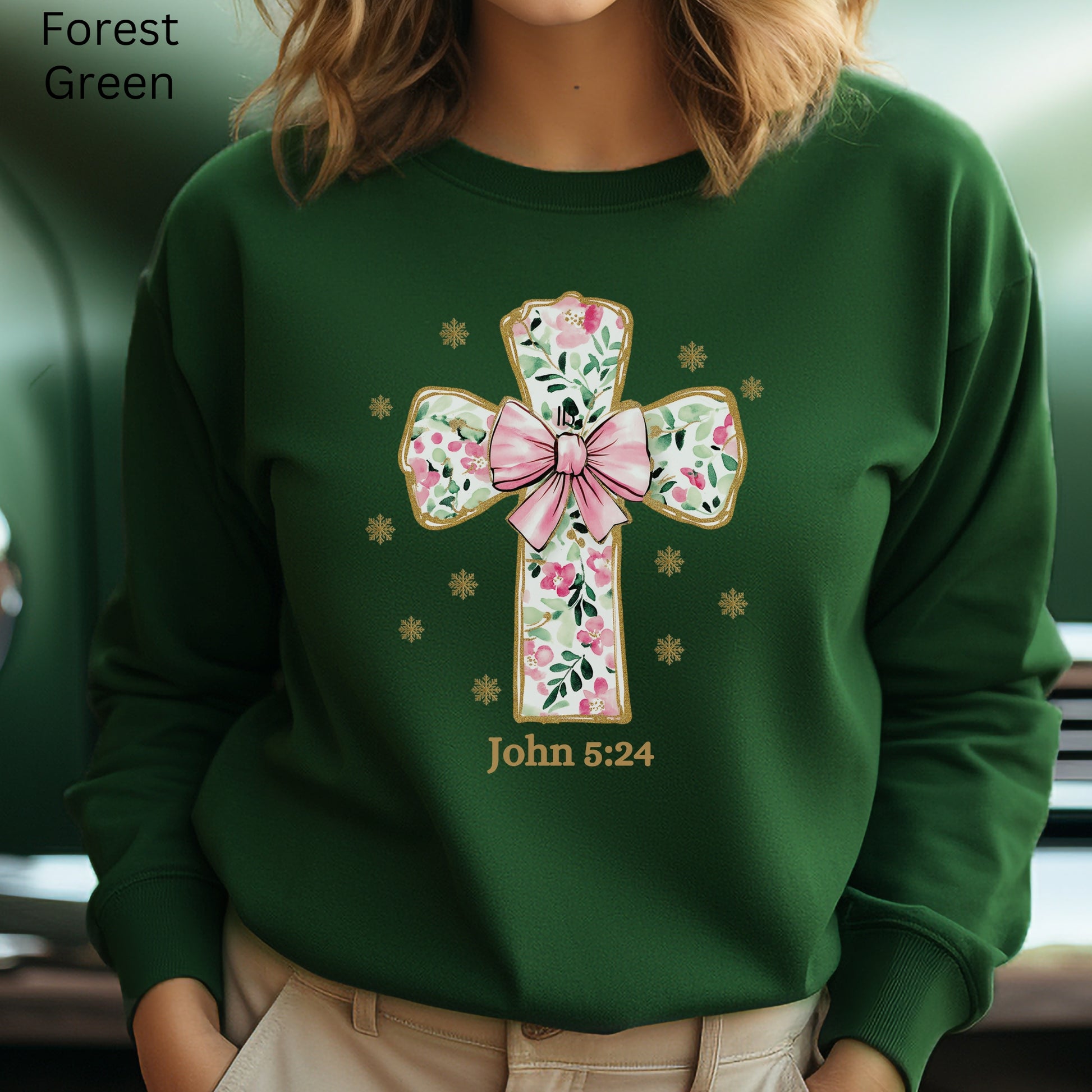 This coquette style Christian cross design on a sweatshirt with pink and green flowers is  decorated with a pink bow. John 5:24 is noted below.